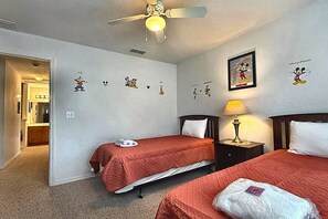 Ein Hotelzimmer mit zwei Betten, einem Deckenventilator und Wandbildern, darunter Mickey Mouse.