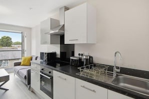 A modern kitchen with white cabinets, a black countertop, and stainless steel appliances. - Spacious Central Flat | Old Trafford (Greater Manchester)