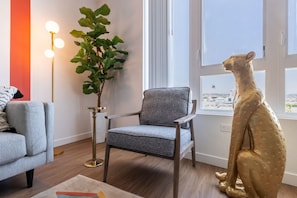 A modern living room with a grey armchair, a floor lamp, a potted plant, and a golden kangaroo statue. - Artsy Space in Lil Tokyo-Free Parking-1Mi to DTLA (Los Angeles)