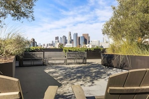 An outdoor seating area with benches and planters, overlooking a city skyline. - Artsy Space in Lil Tokyo-Free Parking-1Mi to DTLA (Los Angeles)