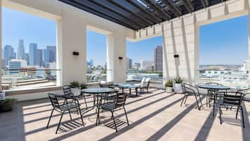 An outdoor terrace with multiple tables and chairs, large windows offering city views, and a pergola structure.