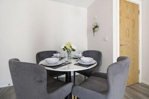 A dining area with a round table, four grey upholstered chairs, and a vase with flowers. - Central Apartment | Parking | Old Trafford (Greater Manchester)
