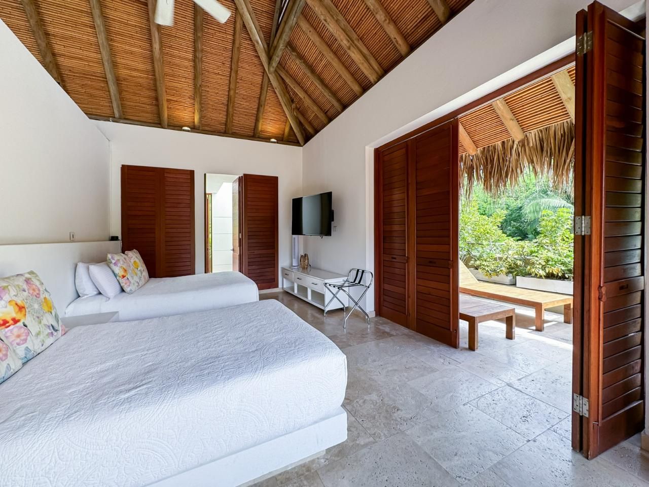 A bedroom with two beds, a TV, a desk, and a view of the garden.