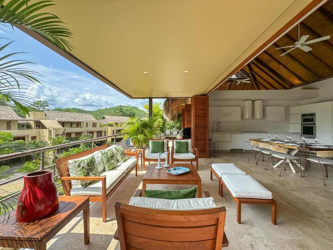 An outdoor patio with wooden furniture, a dining table, and a view of a lush landscape.