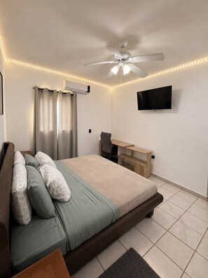 A bedroom with a bed, a desk, a chair, a ceiling fan, and a TV. - New Listing (Monterrey)