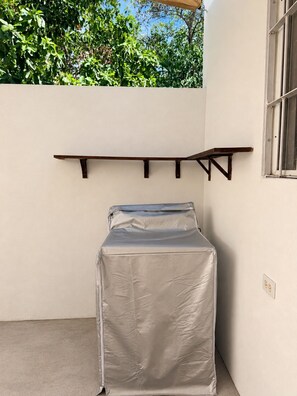A room with a bed covered in a protective sheet, a wooden shelf, and a window with metal bars. - New Listing (Monterrey)