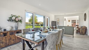 A dining area with a glass table, chairs, and a view of a vineyard through large windows. - Meadow View - outside Cheltenham with hot tub and games room, Sleeps 6 (Sandhurst)