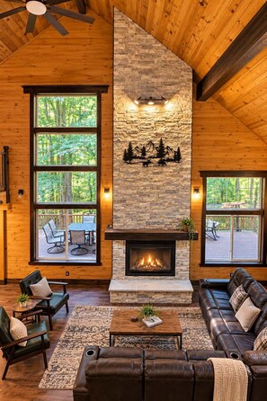 A cozy living room with a stone fireplace, leather furniture, and large windows overlooking a deck.