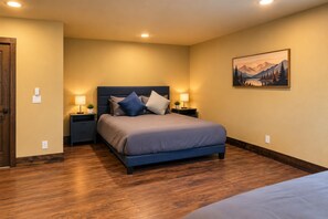 A bedroom with a bed, nightstands, lamps, a painting, and wooden flooring.