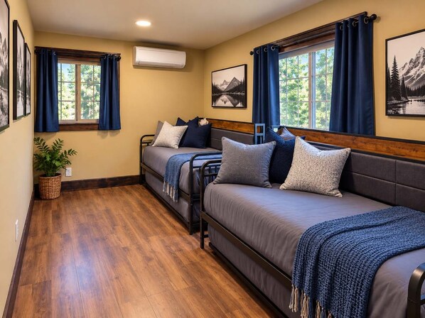 A room with two beds, a potted plant, and artwork on the walls.