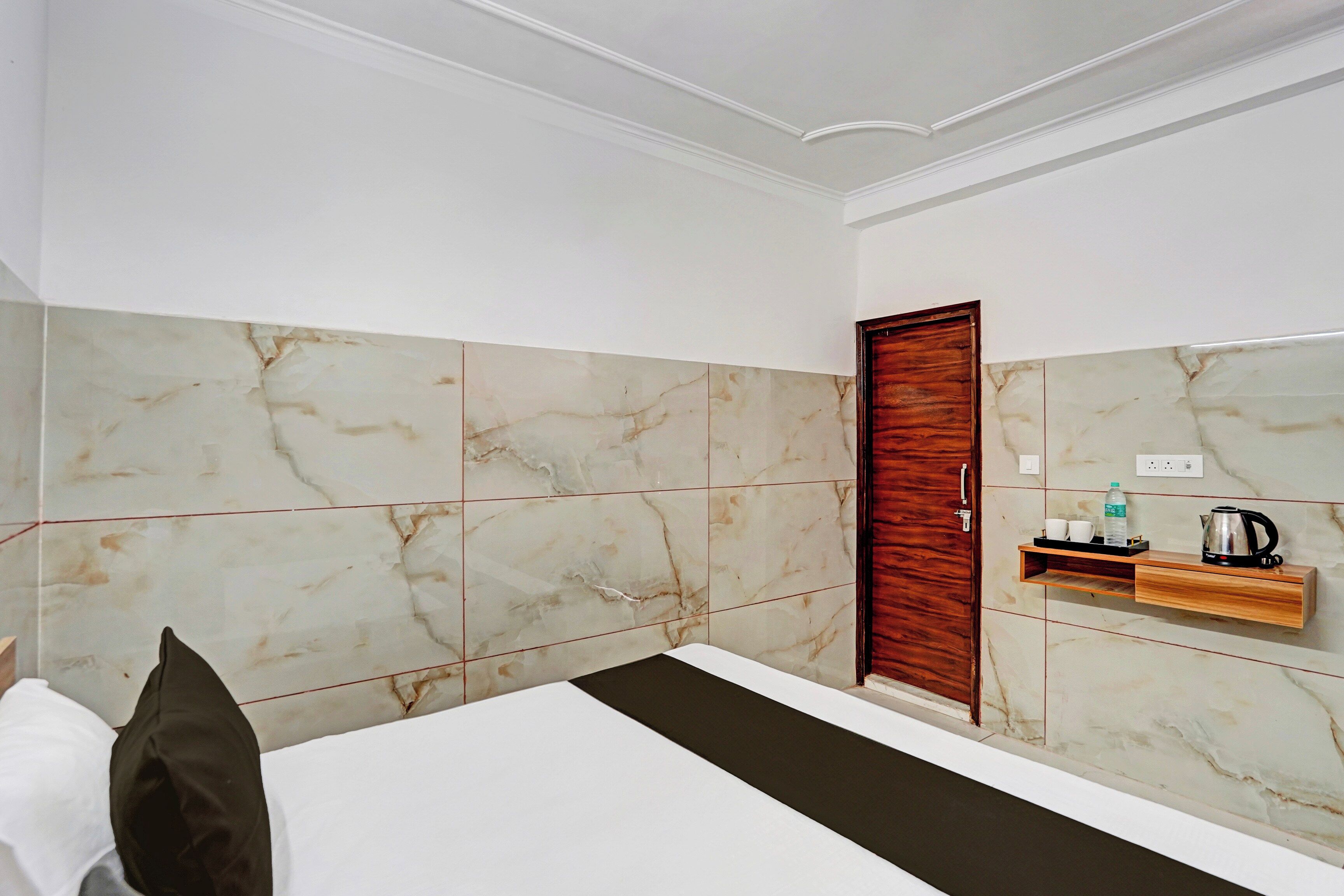 Habitación de hotel con cama, una puerta de madera, un estante con artículos de tocador y una pared de mármol.