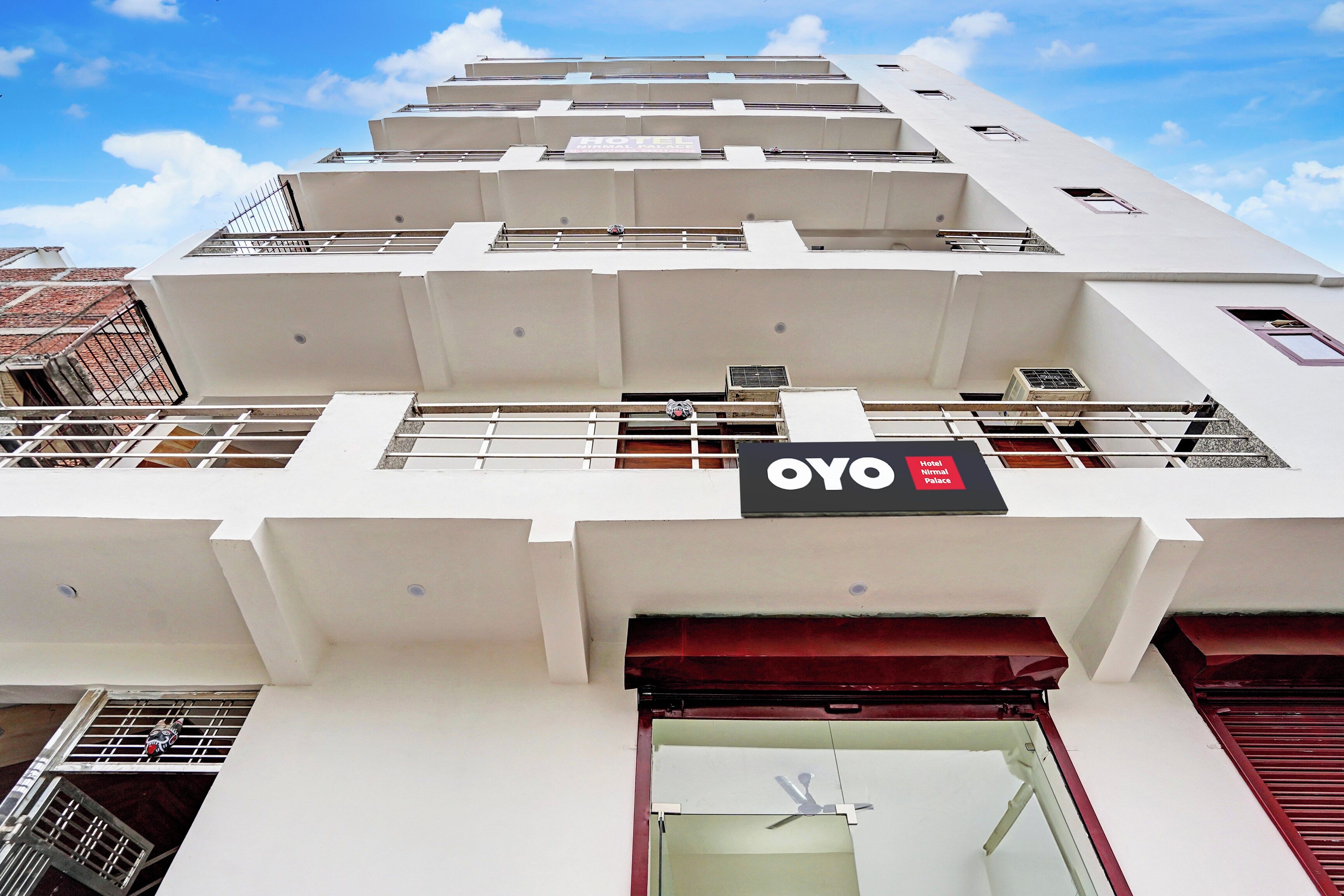 Un bâtiment d’hôtel avec une enseigne indiquant « OYO Hotel Nirmal Palace » et une entrée bien visible, surmontée d’un auvent rouge.