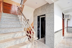 A staircase with a wooden handrail and granite steps leading to a dark doorway. - HOtel O The Clarks Inn (Noida)