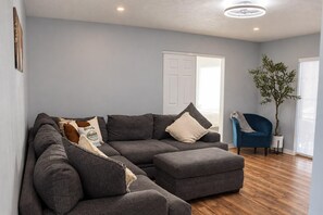 Un salon moderne avec un canapé d’angle, un fauteuil bleu et une plante en pot.