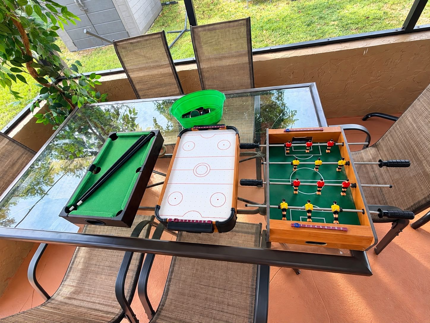 A glass-top table with a pool table, foosball table, and a green paddle table.