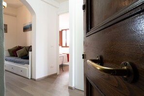 A room with a bed, a desk, and a wooden door with a brass handle. - New Listing (Lucca)
