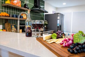 A kitchen counter with a bottle of wine, two glasses of red wine, a piece of cheese, grapes, and a wooden cutting board. - Walkable SoBro house near Broadway, sleeps 8, funky decor throughout (Nashville)