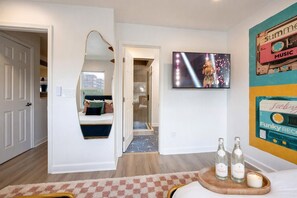 Habitación de hotel con cama, televisión, espejo y un cuadro con temática musical en la pared.