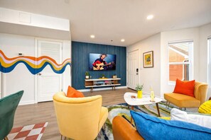 A living room with a television, a sofa, a coffee table, and a patterned rug. - Walkable SoBro house near Broadway, sleeps 8, funky decor throughout (Nashville)