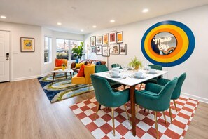 A modern living room with a dining area, featuring a checkered rug, a neon sign, and framed artwork on the walls. - Walkable SoBro house near Broadway, sleeps 8, funky decor throughout (Nashville)