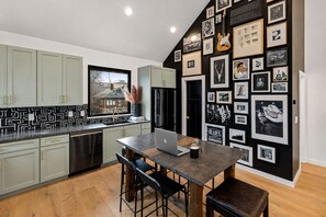 A modern kitchen with a dining area, featuring a laptop on the table, a coffee cup, and framed pictures on the wall. - Nashville house with private rooftop patio near Broadway, sleeps 12 (Nashville)
