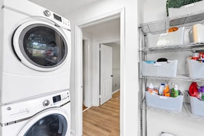 A laundry area with stacked washing machines and shelves with cleaning supplies. - Fall getaway: 1920s craftsman house, sleeps 10, fenced yard, East Nashville (Nashville)