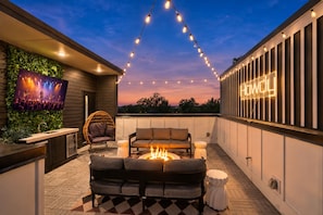 An outdoor patio with a fire pit, seating, a television, and string lights. - Rooftop fire pit & game room, sleeps 10 near downtown Nashville & Broadway (Nashville)