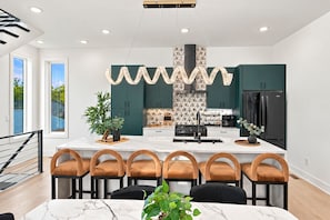 A modern kitchen with a central island, dark green cabinets, and a black refrigerator. - Rooftop fire pit & game room, sleeps 10 near downtown Nashville & Broadway (Nashville)
