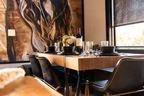 A dining area with a wooden table set for four, black chairs, a wine bottle, and a vase with flowers. - Fall in Nashville: skyline-view house, 4 ensuite baths, sleeps 12 (Nashville)