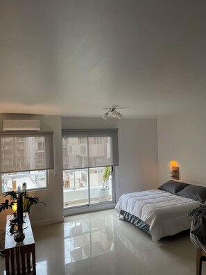 A bedroom with a bed, a bedside table, a window with a view of the outside, and a ceiling fan. - New Listing (Buenos Aires)