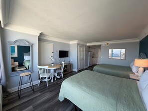 A hotel room with two beds, a desk with a chair, a television, and a window with a city view. - Studio Beach Access Studio Kitchen Amazing Location (Daytona Beach)