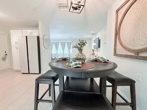 A modern kitchen with a round dining table, two barstools, a refrigerator, and a decorative mirror. - Serene 2BR with Expansive Backyard Oasis (St. Petersburg)