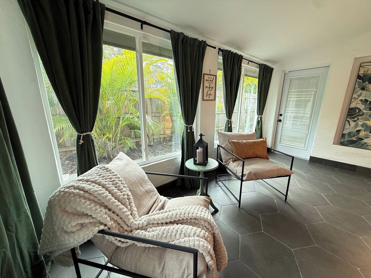 A room with a sofa and armchair, a small table with a candle, and a window with curtains.