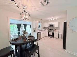 A modern kitchen with white cabinets, a dining area with a round table, and a view of the outdoors. - Serene 2BR with Expansive Backyard Oasis (St. Petersburg)