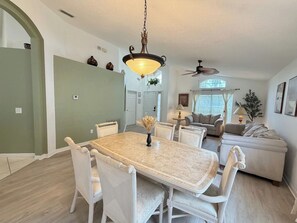 A dining area with a marble table and white chairs, a chandelier, and a ceiling fan. - Greek Villa w/ Sunny Pool just 20 Min to Disney (Kissimmee)