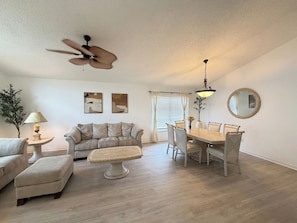 A living room with a sofa, ottoman, dining table, chairs, ceiling fan, and a lamp. - Greek Villa w/ Sunny Pool just 20 Min to Disney (Kissimmee)