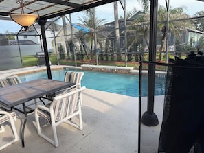 Ein Poolbereich im Freien mit Tisch und Stühlen, einer Pergola mit Lampe und Blick auf eine Wohngegend.