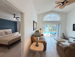 A hotel room with a bed, a sitting area with a table and chairs, a ceiling fan, and a view of the outdoors. - Greek Villa w/ Sunny Pool just 20 Min to Disney (Kissimmee)