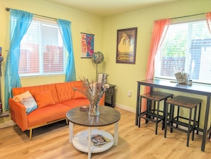 A living room with a sofa, a coffee table, a dining table with chairs, and a window with curtains. - Private, comfy, colorful 2 bed 2 bath home close to everything (Sacramento)