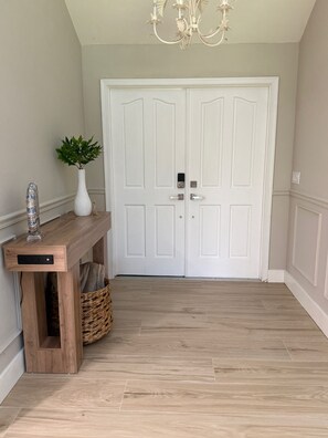 Un couloir avec une porte double blanche, une console en bois sur laquelle sont posés un vase et une plante, et un panier en osier.