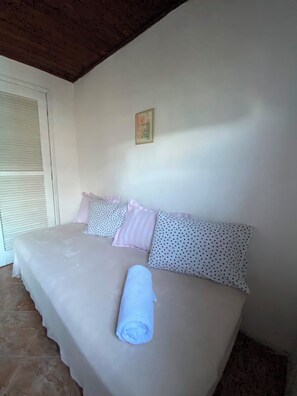 A bedroom with a bed, pillows, a rolled towel, a window with blinds, and a picture on the wall. - New Listing (Arraial do Cabo)