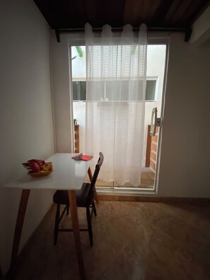 A dining area with a table and chairs, a window with a sheer curtain, and a view of a building outside. - New Listing (Arraial do Cabo)