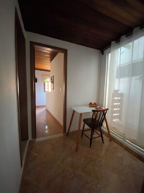 A room with a tiled floor, a white table with a chair, a wooden ceiling, and a window with blinds. - New Listing (Arraial do Cabo)
