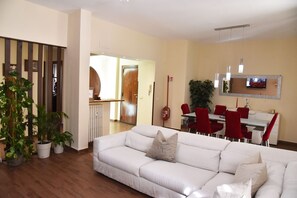 A living room with a white sofa, red chairs, a dining table, and a kitchen area in the background. - Jireh vacation home - Two Bedroom Apartment, Sleeps 5 (Rome)