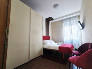 A hotel room with a bed, a red chair, a desk, and a window with curtains. - Jireh vacation home - Two Bedroom Apartment, Sleeps 5 (Rome)