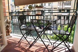 A balcony with two chairs and a table, a potted plant, and a view of a street with parked cars. - Jireh vacation home - Two Bedroom Apartment, Sleeps 5 (Rome)