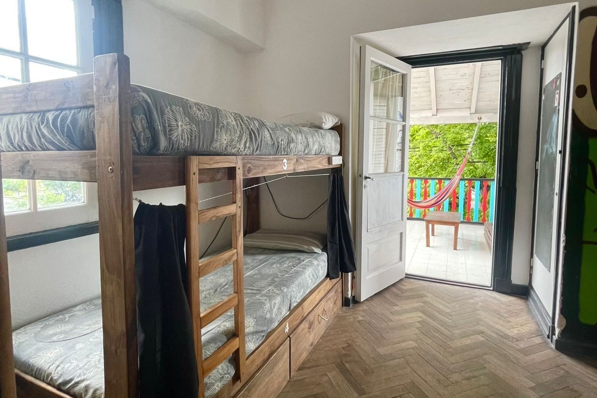 A room with two bunk beds, a wooden floor, and a door leading to an outdoor area with a hammock.