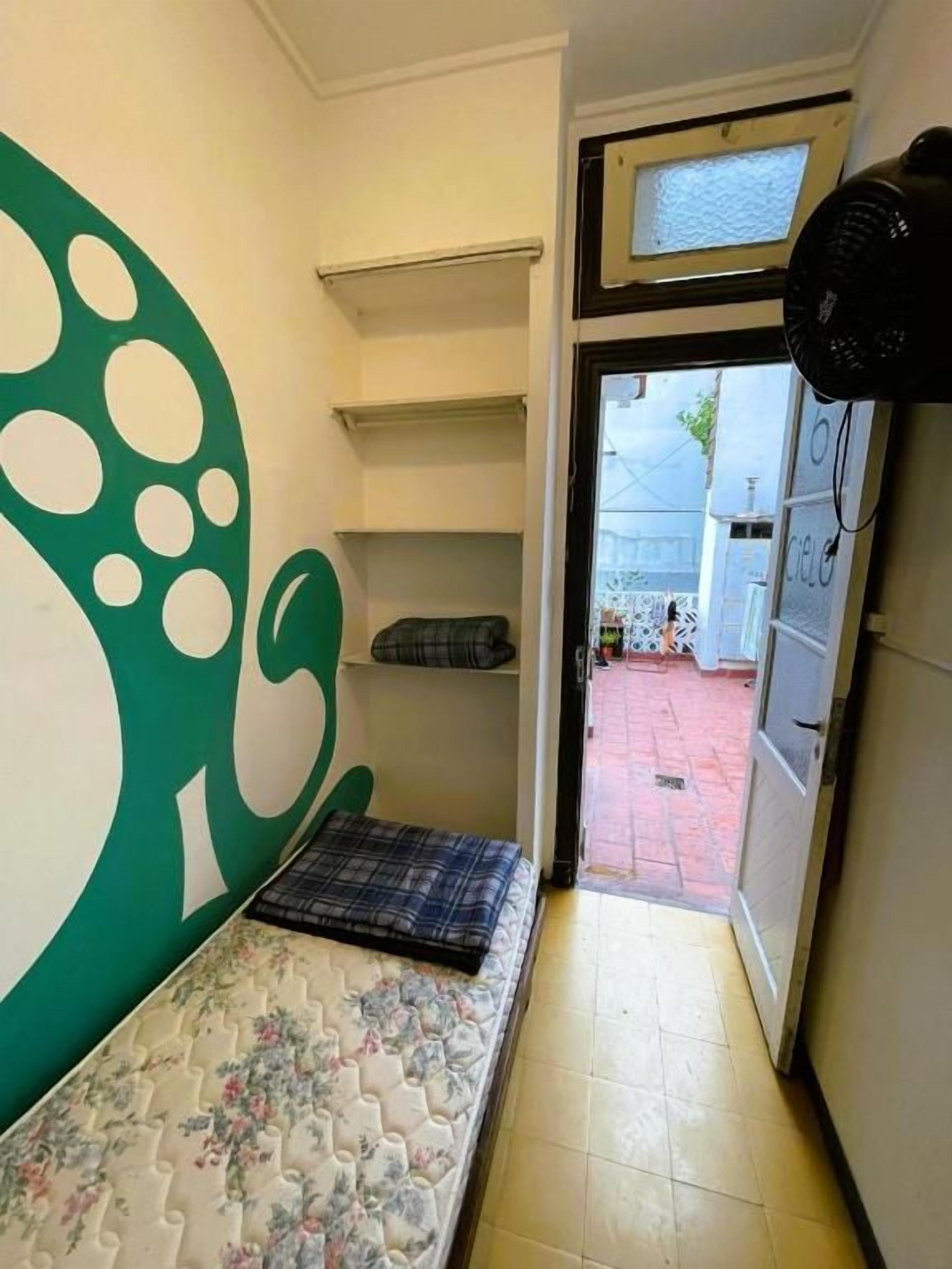 Ein schmaler Flur mit einem Bett, einer grünen Wand mit einer großen weißen Zahl und einer zur Außenseite führenden Tür.