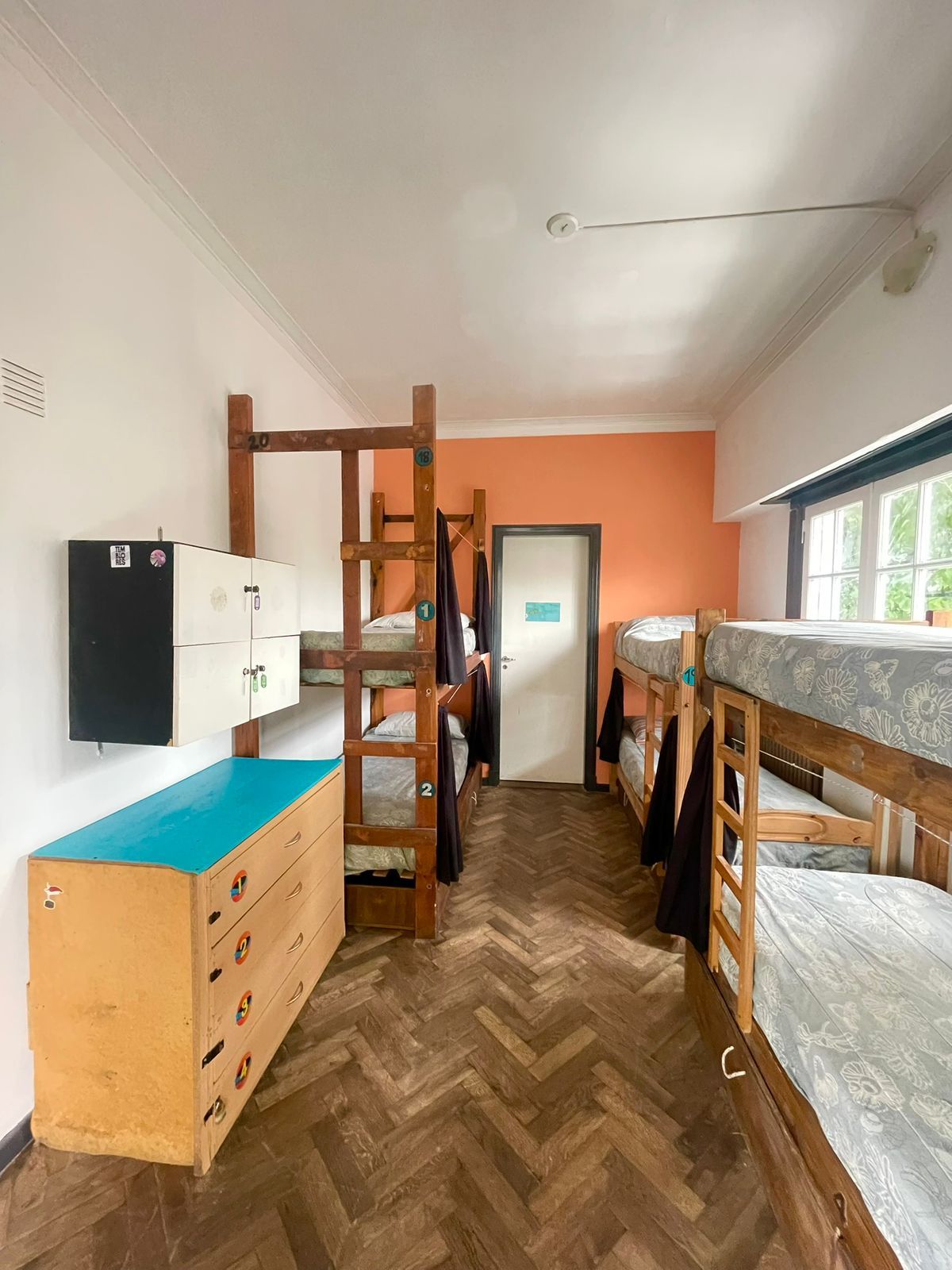 A dormitory room with bunk beds, a dresser, a wardrobe, and a window with a view.