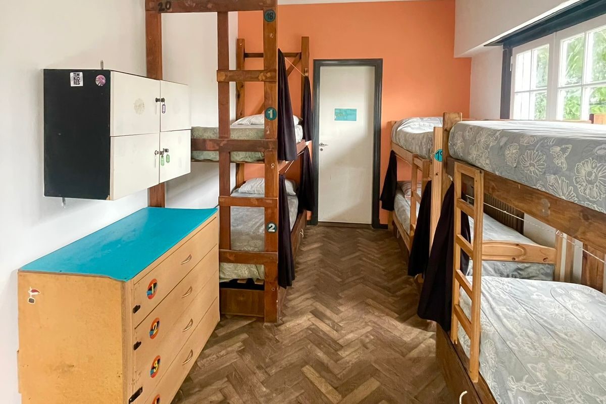 A dormitory room with bunk beds, a dresser, a wardrobe, and a window with a view.